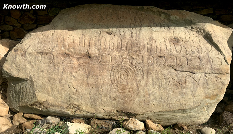 Knowth Kerbstone K52 with a picket-fence zigzag top, a row of U-shapes, a central multi-ring spiral, and concentric circles upper right.